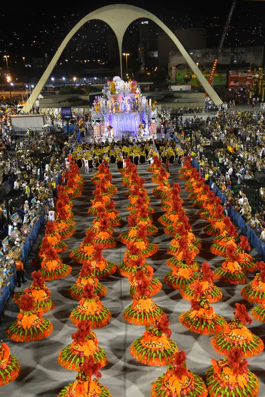 Desfile de Carnaval com dançarinas coloridas e multidão assistindo.