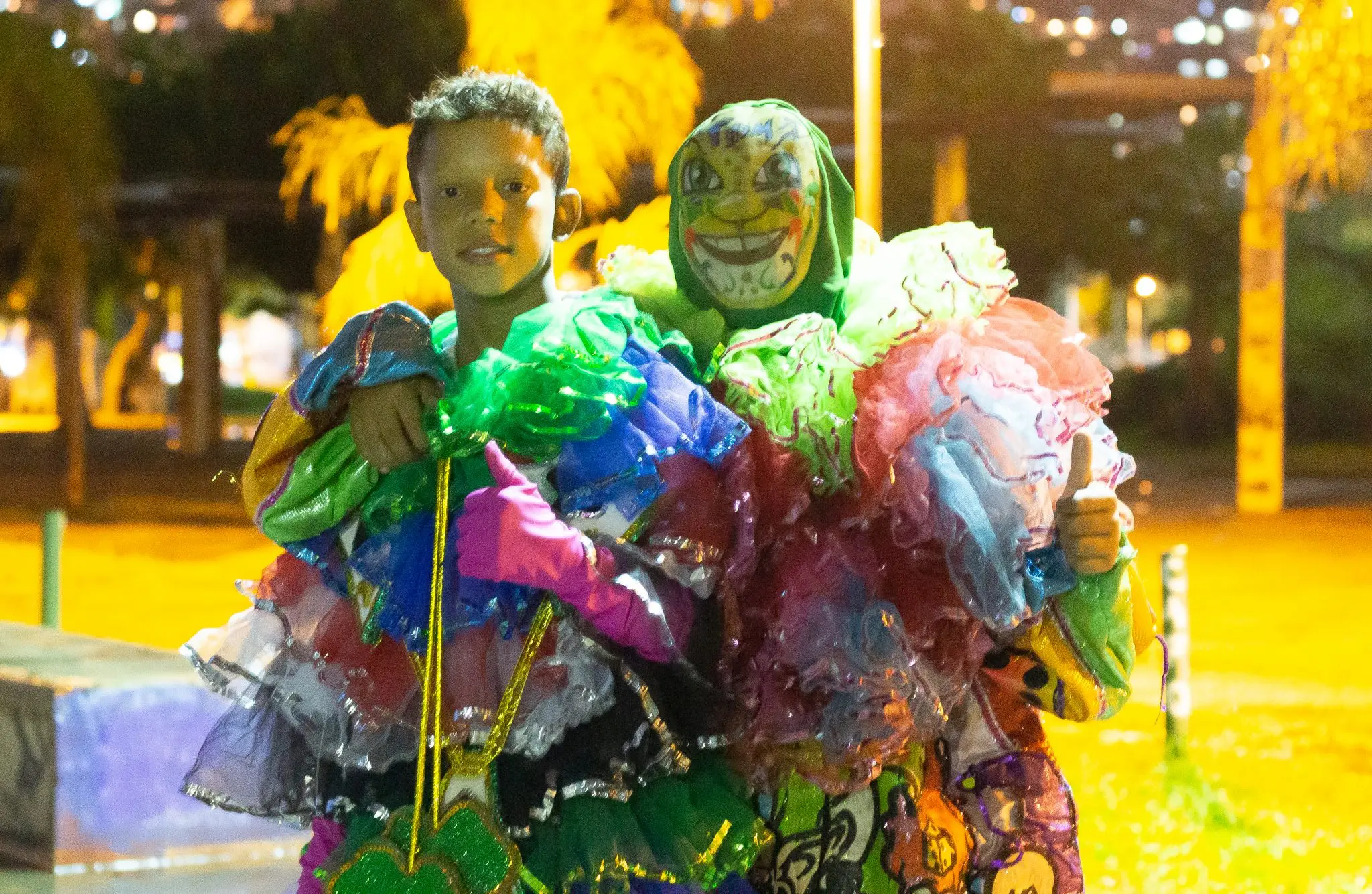 Criança sorridente segurando boneco festivo em evento noturno.