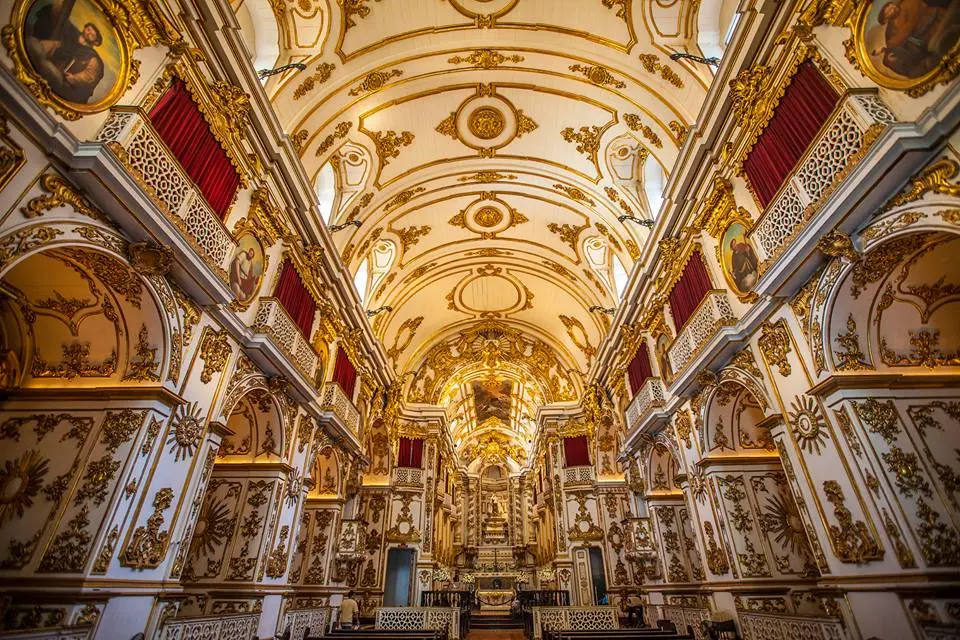Interior ornado de igreja com detalhes dourados e painéis vermelhos.