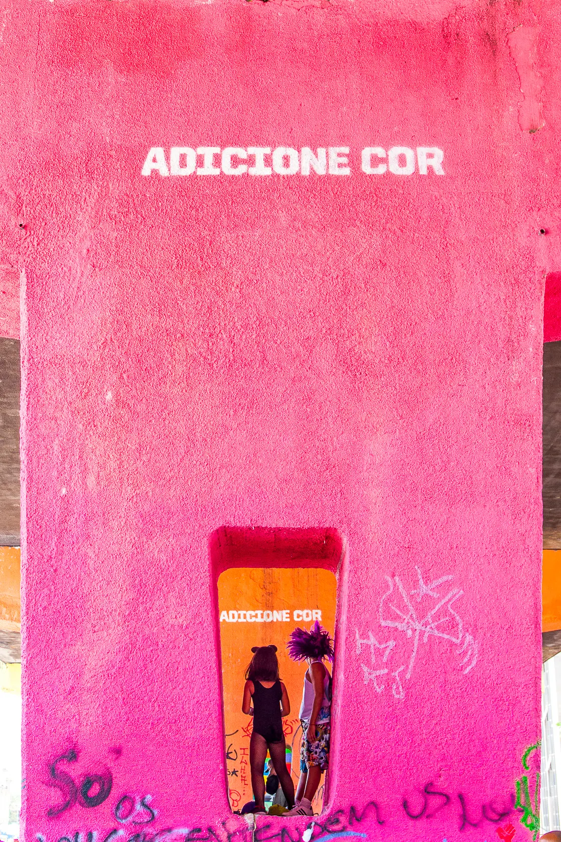 Parede rosa vibrante com frase "ADICIONE COR" e espelho refletindo duas pessoas de costas.
