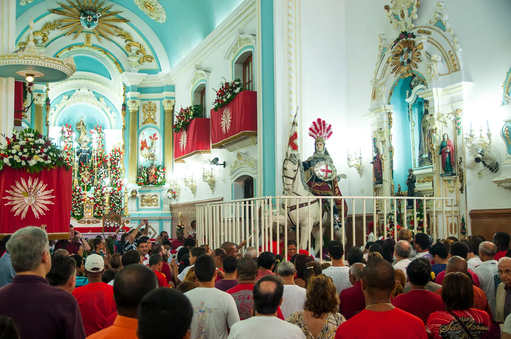 Cerimônia religiosa em templo com decoração floral e figura montada em cavalo.