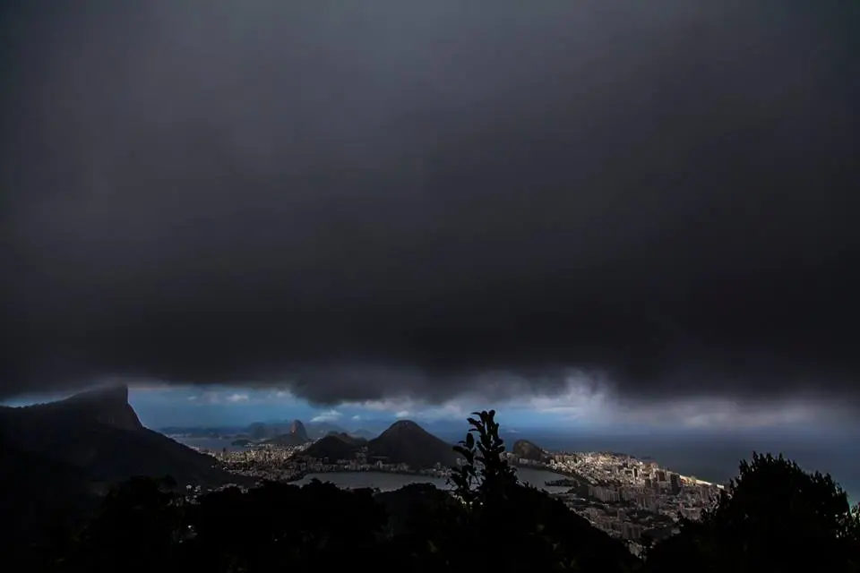 Paisagem urbana sob céu nublado com montanha e água.