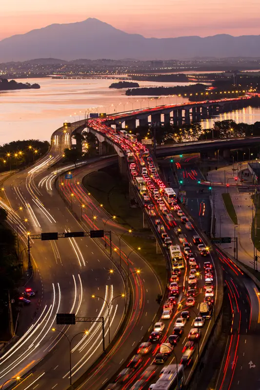 Vista aérea da Linha Vermelha durante o crepúsculo, com tráfego congestionado e paisagem distante.