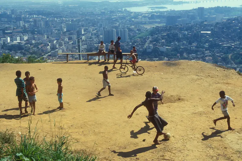 Jovens jogando futebol em morro com vista para Rio de Janeiro.