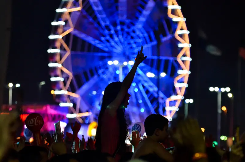 Fotografia de evento noturno com roda-gigante e multidão animada.