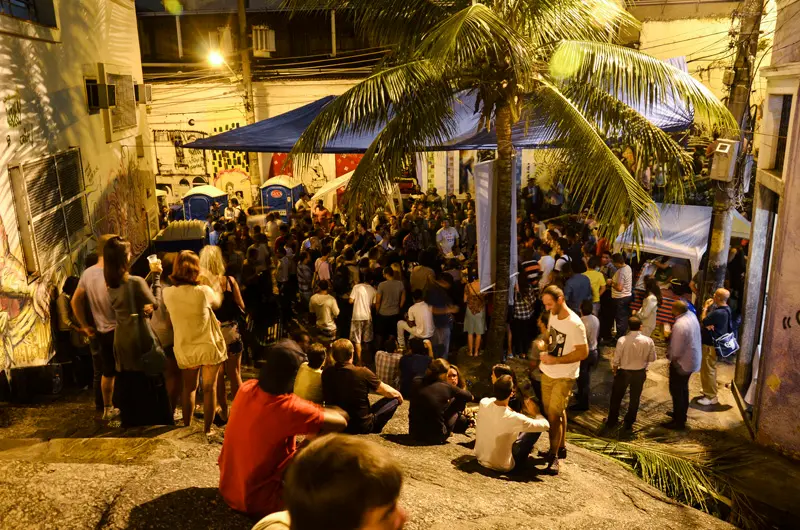 Multidão em samba na Pedra do Sal, noite, grafites, palmeira, barracas azuis.