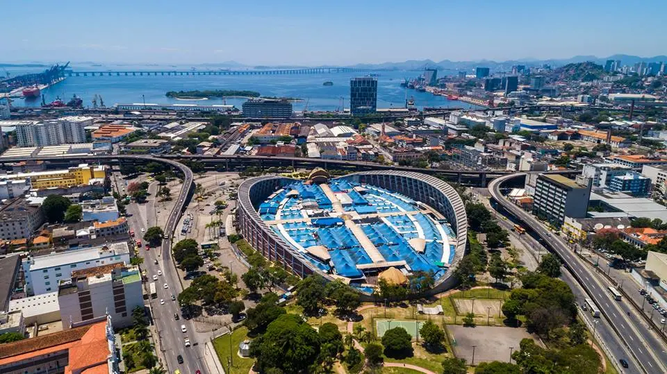 Cidade costeira com edifícios, complexo esportivo e ponte sobre o mar.