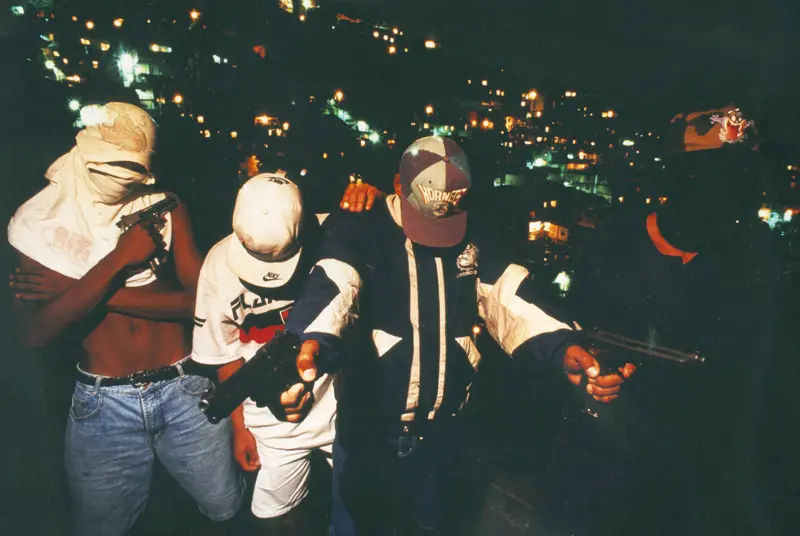 Três homens armados em uma cidade noturna.