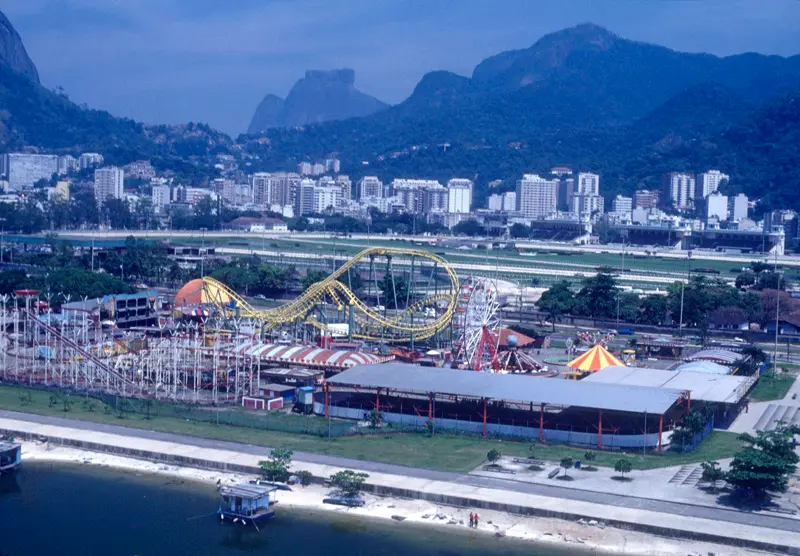 Parque de diversões colorido com montanha-russa e palco azul.