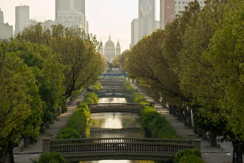 Canal fluvial em cidade com árvores e edifícios modernos ao fundo.