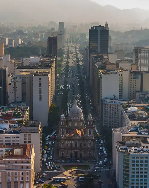 Cidade com tráfego, edifícios modernos e antigos, igreja, montanhas nebulosas.