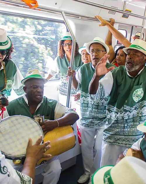 Grupo de pessoas em ônibus tocando instrumentos, uniformes verdes.