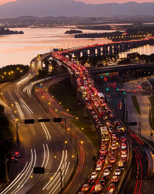 Vista aérea da Linha Vermelha durante o crepúsculo, com tráfego intenso e ponte iluminada.