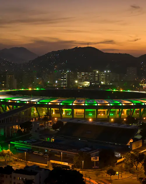 Estádio iluminado à noite com cidade ao fundo.