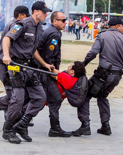 Policiais arrastando manifestante em meio a multidão.