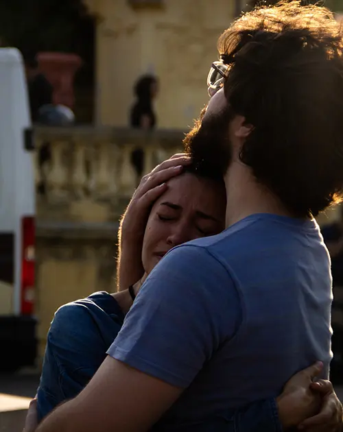 Dois amigos abraçados em cidade, um chorando.