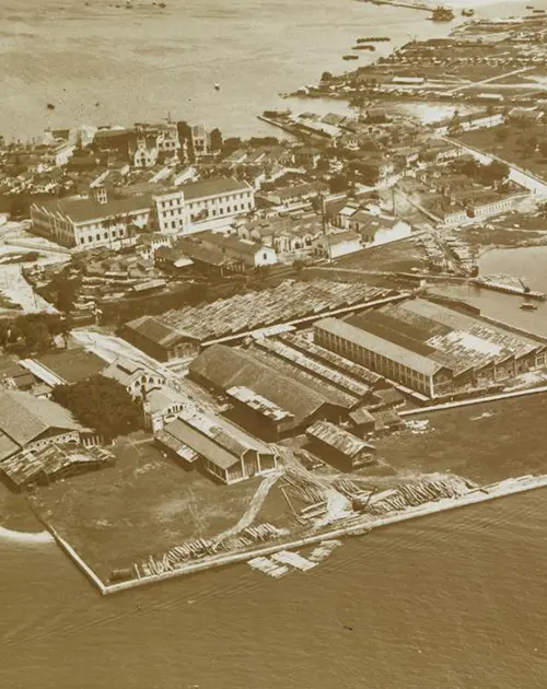 Área industrial perto do mar, com edifícios industriais e pilhas de madeira.