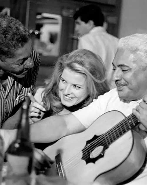 Três pessoas em ambiente interno, duas tocam guitarra.
