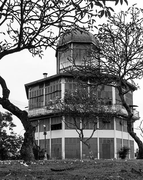 Edifício arredondado com torre pontiaguda, árvores e areia arenosa.