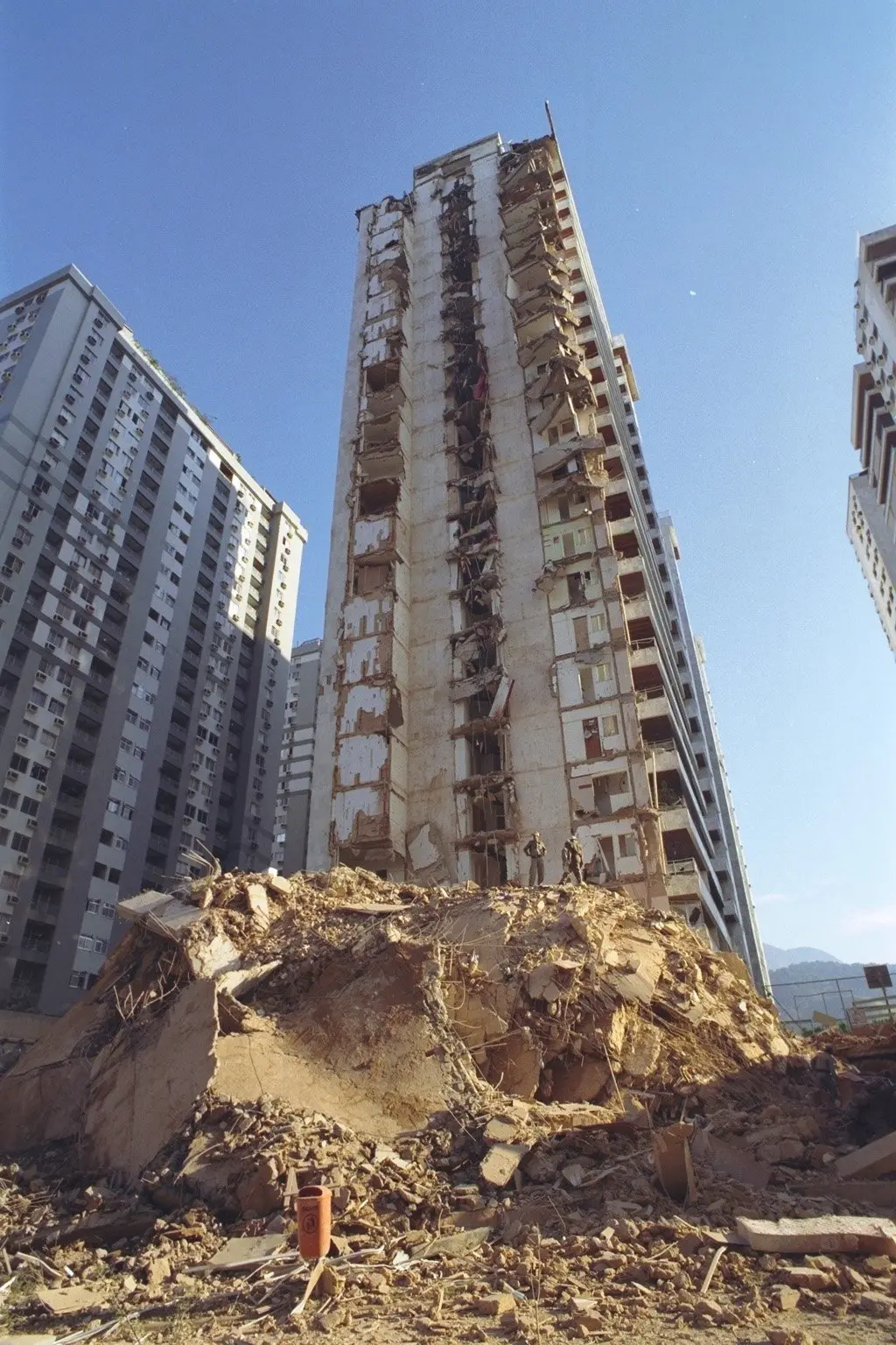 Prédio em ruínas em área urbana, com edifícios residenciais ao fundo.
