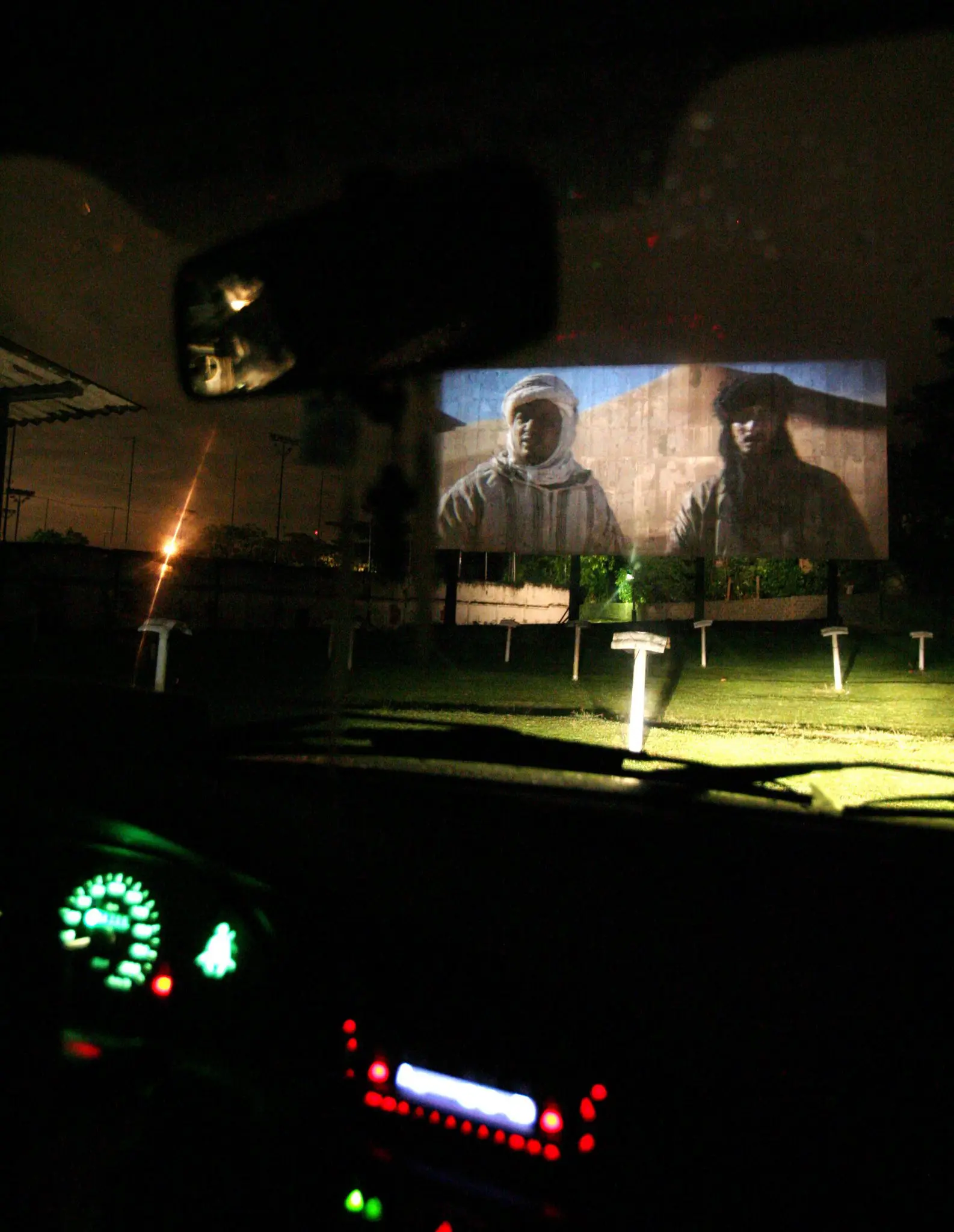 Drive-in à noite com carro iluminado e telhado iluminado.