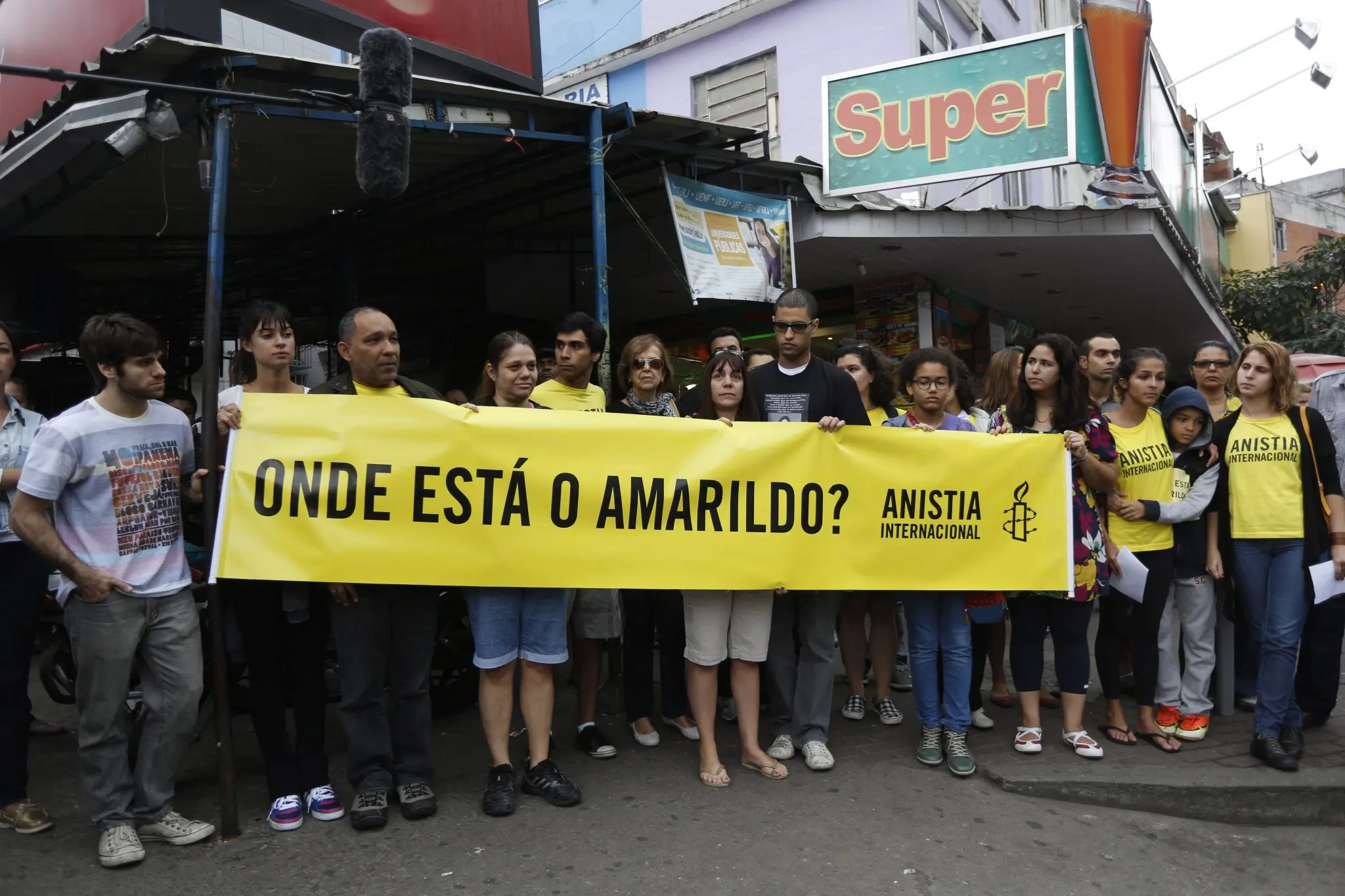Grupo de pessoas segurando banner amarelo em frente ao Super.