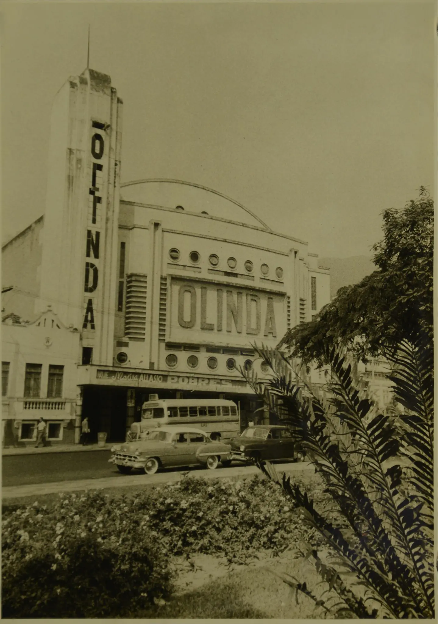 Teatro Olinda em preto e branco, com pessoas e carro na frente, árvore e jardim à direita.