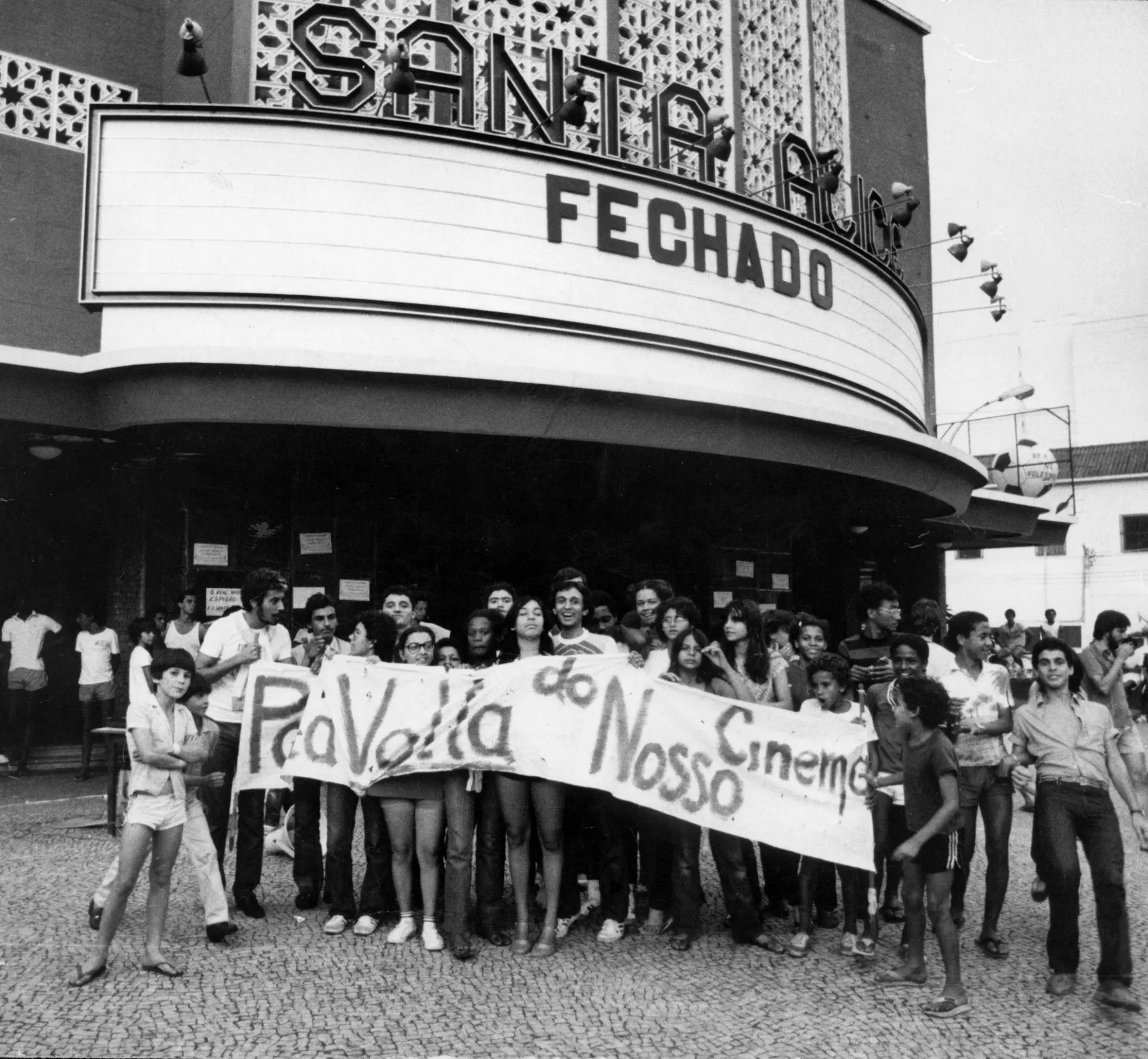 Grupo de pessoas segurando cartaz em frente ao cinema Santa Alice, fechado.