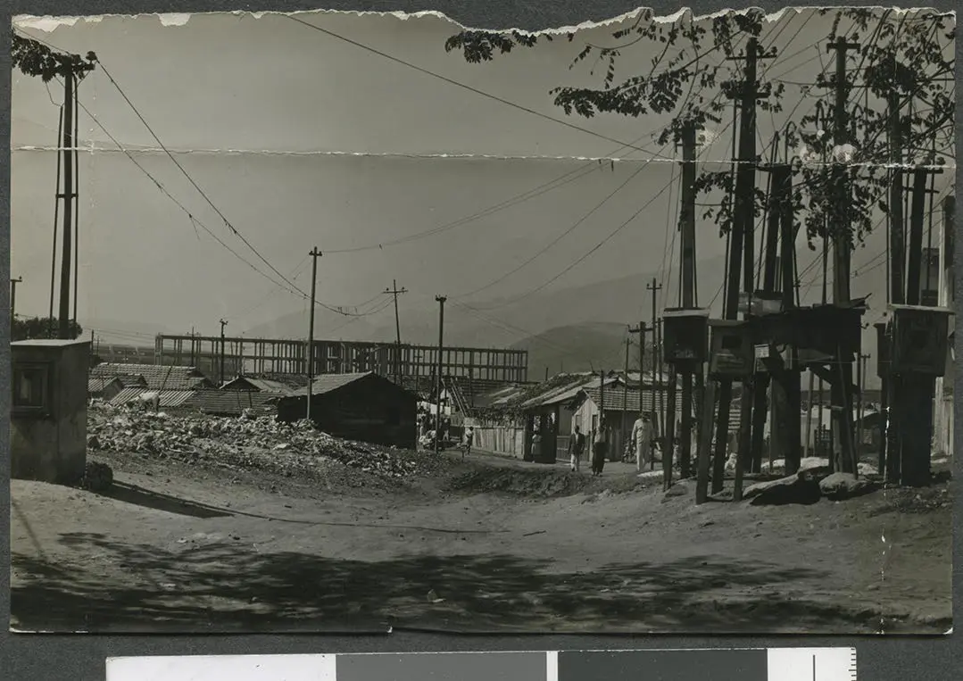 Fotografia preto e branco de favela com construções de tijolos, casinhas de madeira e barracas.