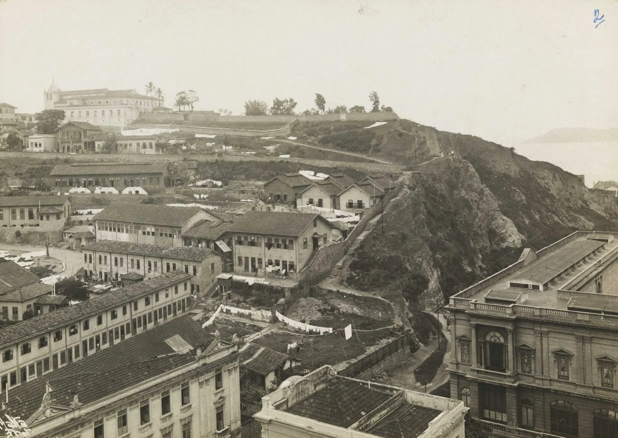 Cidade histórica em preto e branco, com fortaleza central e colina ao fundo.