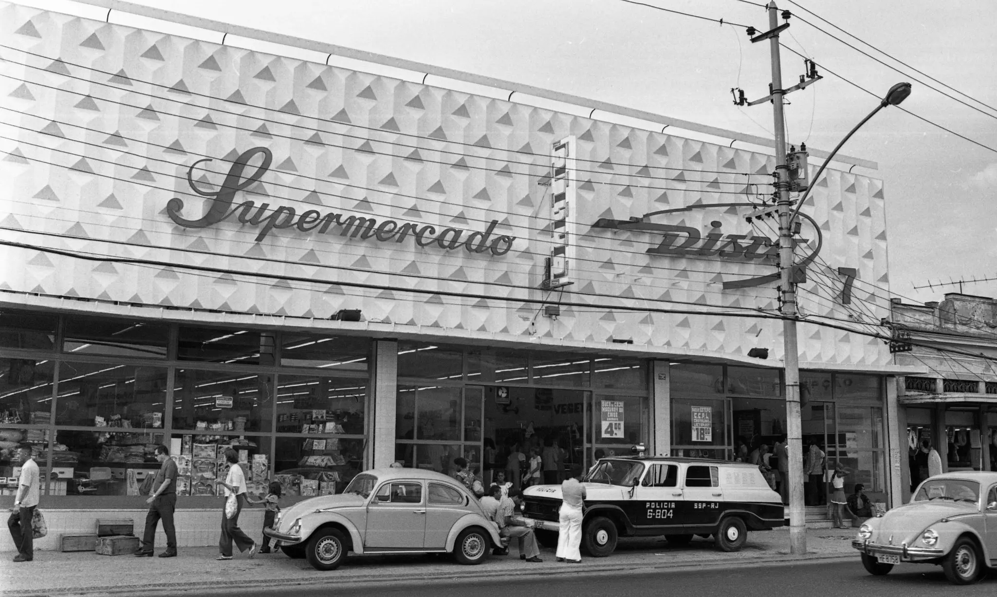 Fachada de supermercado "Disco" com pessoas e carros ao redor.