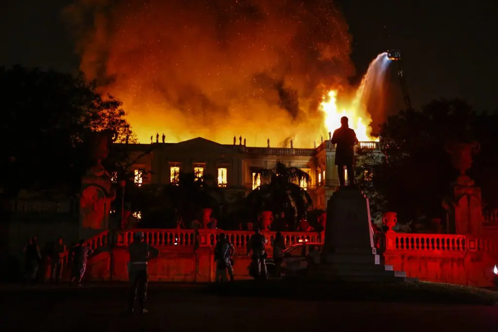 Incêndio noturno em edifício monumental, chamas intensas e fumaça densa.