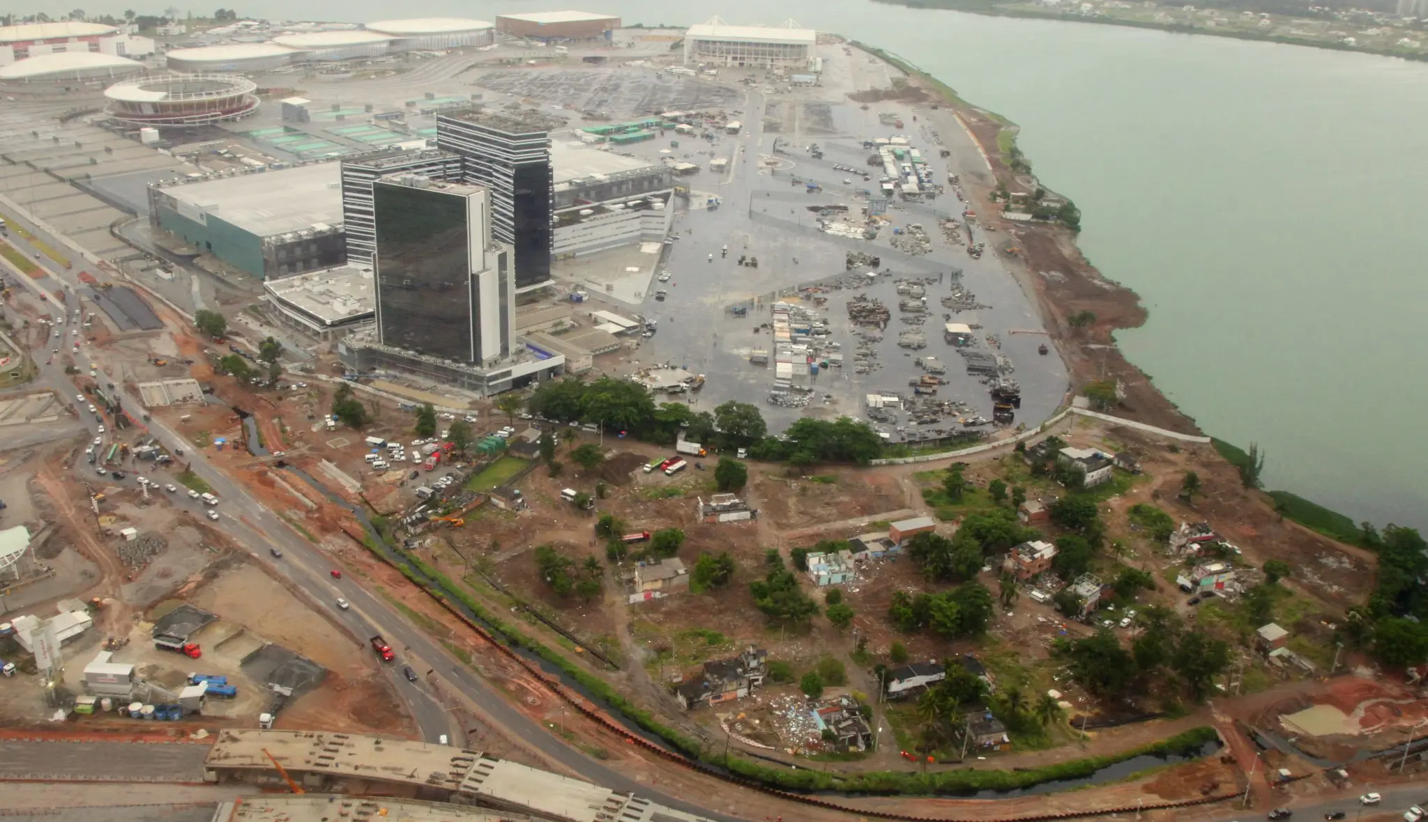 Área urbana em desenvolvimento perto de rio, com edifício moderno e áreas verdes.