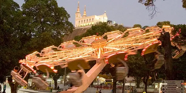 Parque de diversões à noite com roda-gigante e igreja histórica.