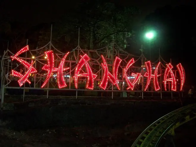 Letreiro vermelho "Shanghai" em parque noturno.