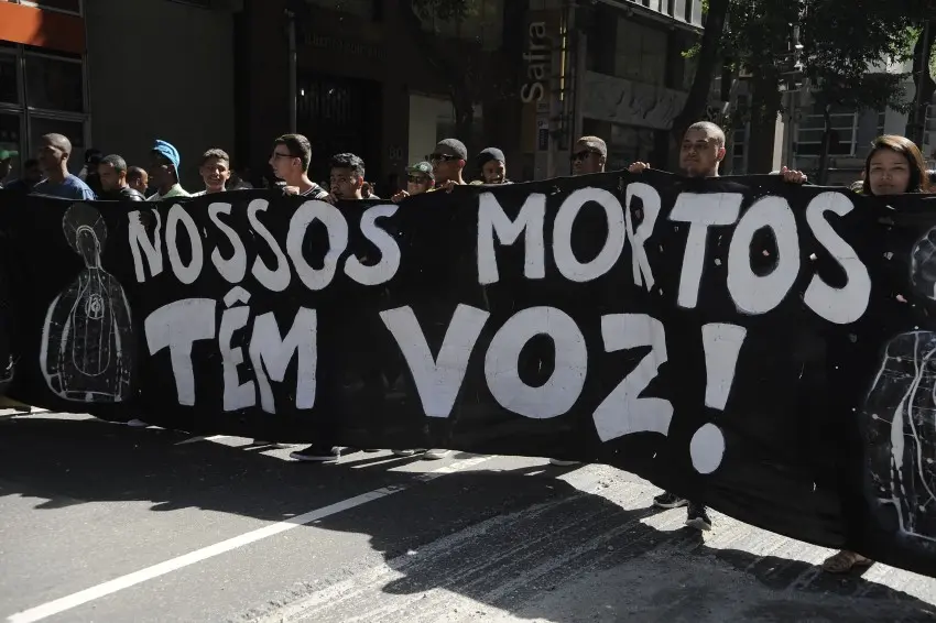 Protesto com cartaz preto e pessoas alvo de tiros.
