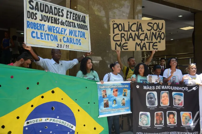 Manifestação pública em frente a edifício com cartazes e bandeira.