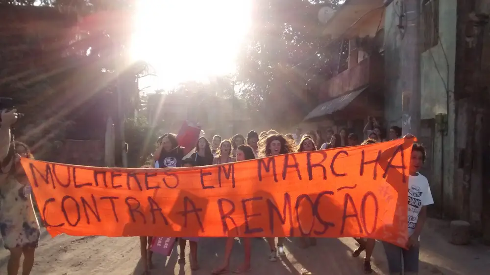 Manifestação de mulheres contra remoção, com cartaz laranja.