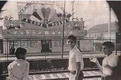 Três pessoas em frente a um teatro de revista, com expressões variadas.