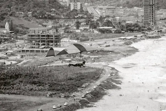 Hang glider em voo sobre praia e vegetação em São Conrado, anos 1970.