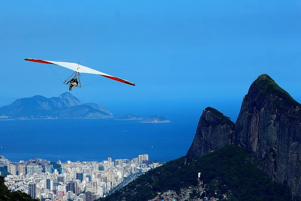 Hang glider voando sobre paisagem urbana e montanhosa.