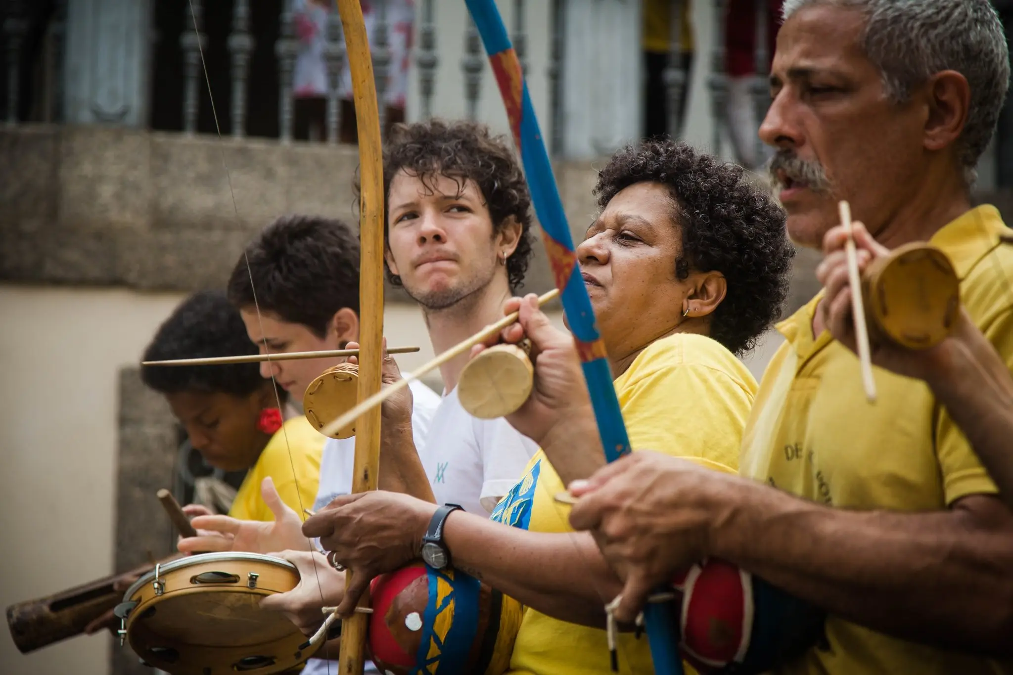 Grupo de pessoas participando de atividade cultural, segurando instrumentos de capoeira.