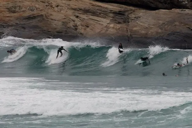 Surfistas na água com ondas grandes e rochas ao fundo.