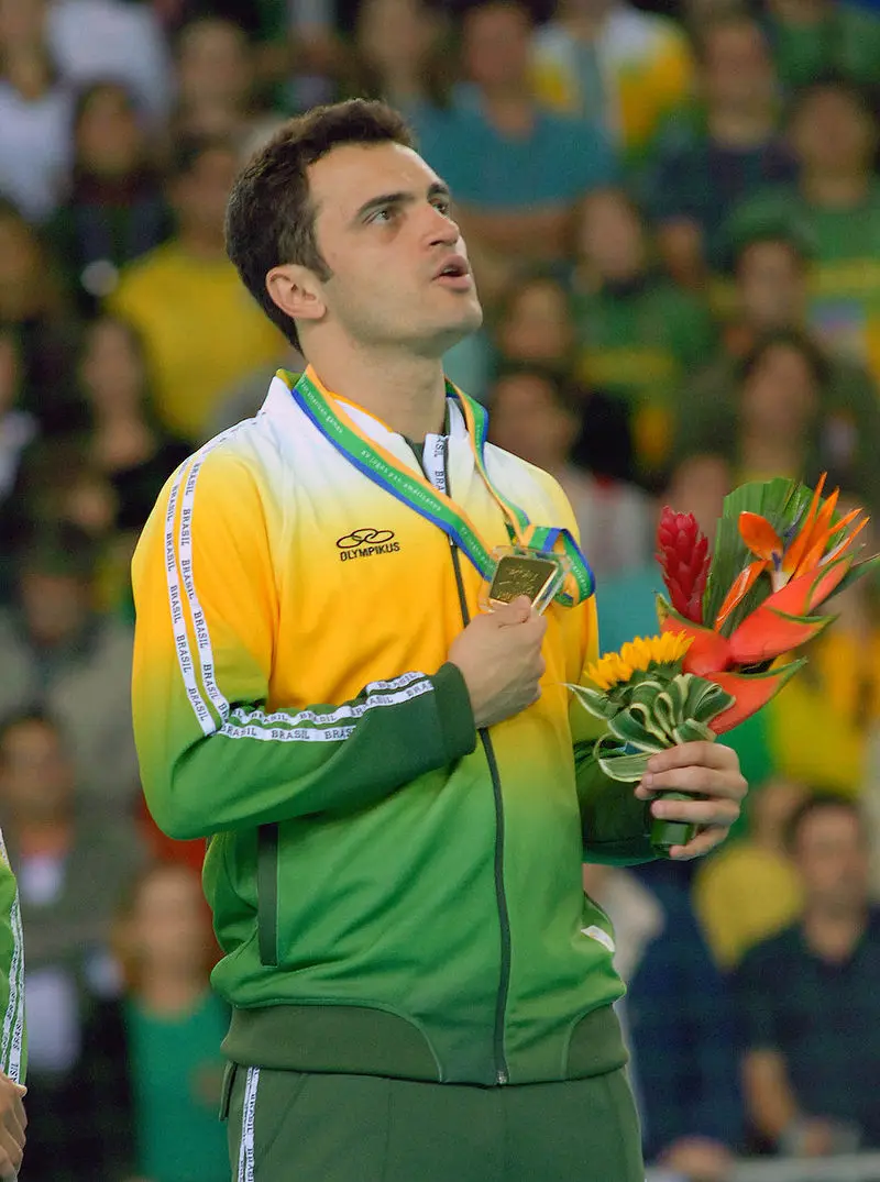 Atleta com medalha de ouro e flores, cerimônia de premiação em estádio.