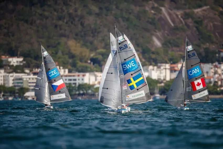 Regata de vela com veleiros marcados com bandeiras da Chequia, Suécia e Canadá.