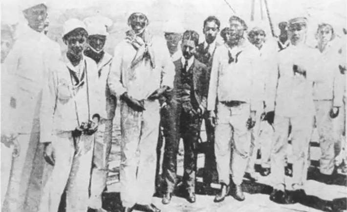 Grupo de pessoas em pé lado a lado, roupas casuais, alguns sorriem para a câmera.