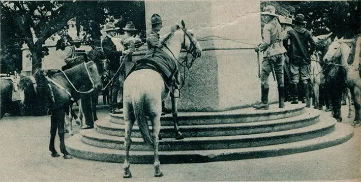Grupo de soldados montando cavalos em frente a monumento.