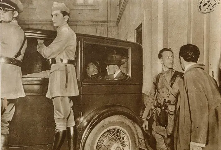 Grupo de pessoas ao redor de um carro clássico em preto e branco.