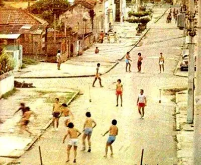 Rua antiga com crianças jogando futebol.