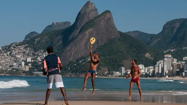 Três amigos na praia, montanhas ao fundo.
